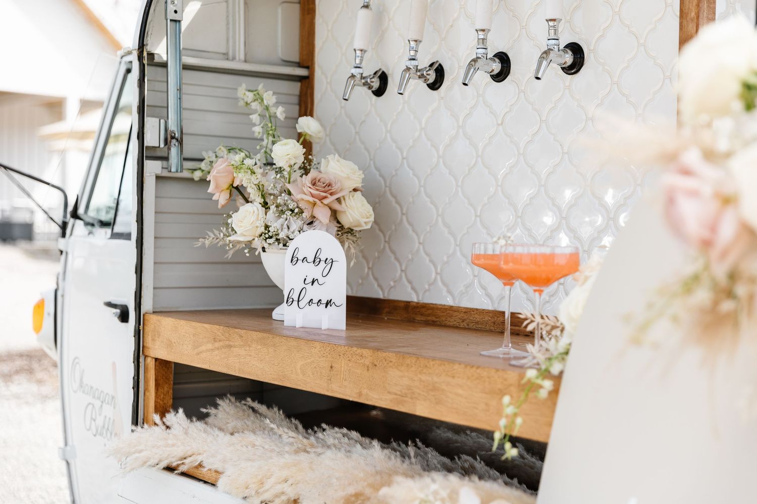 A mobile bar setup with a wooden counter, floral arrangements, and cocktail glasses in a rustic vintage camper.