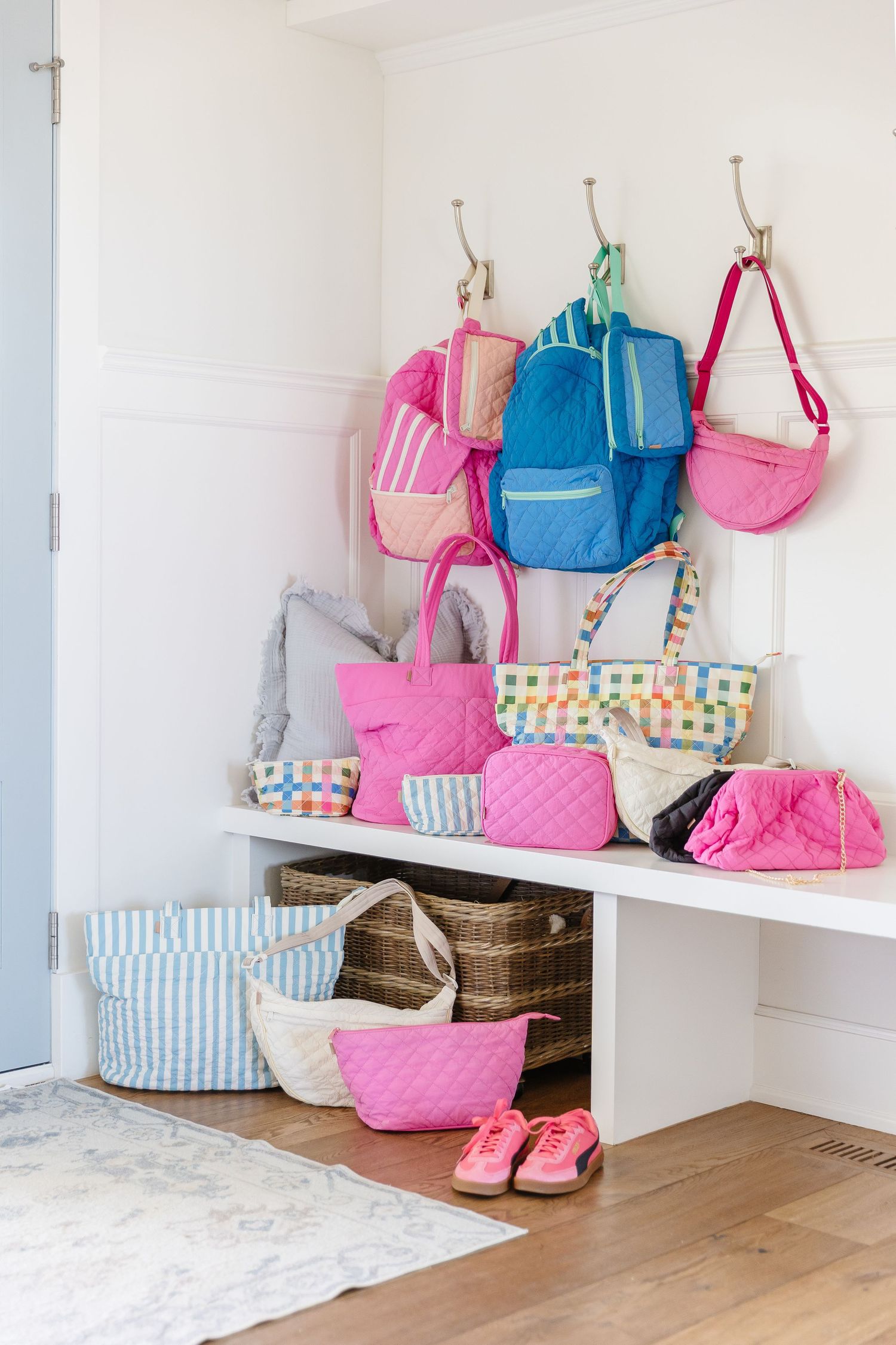 Colorful backpacks and bags in pink and blue tones arranged neatly on white shelving units with wooden flooring below.