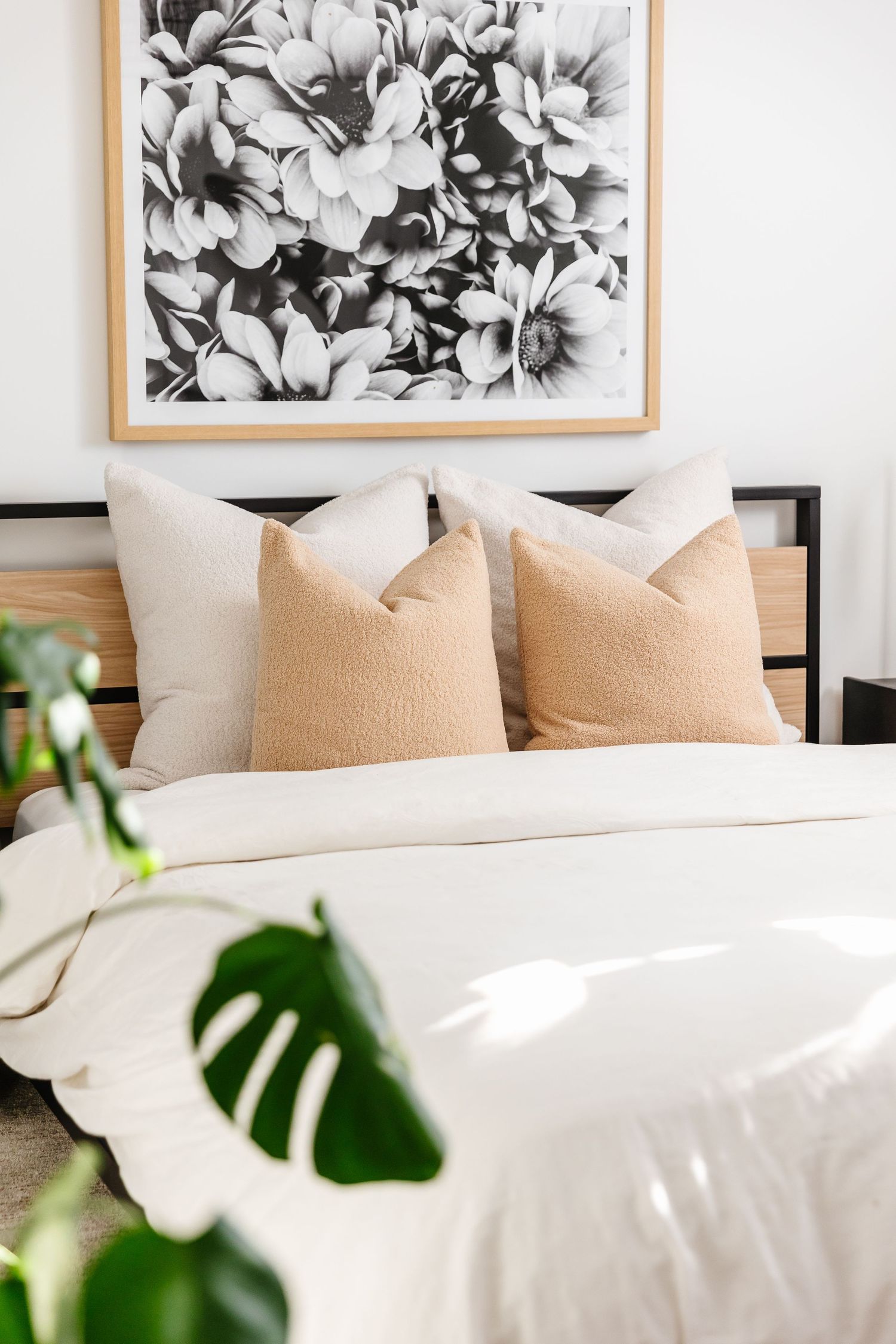 Black and white floral artwork above a bed with beige pillows and white bedding.
