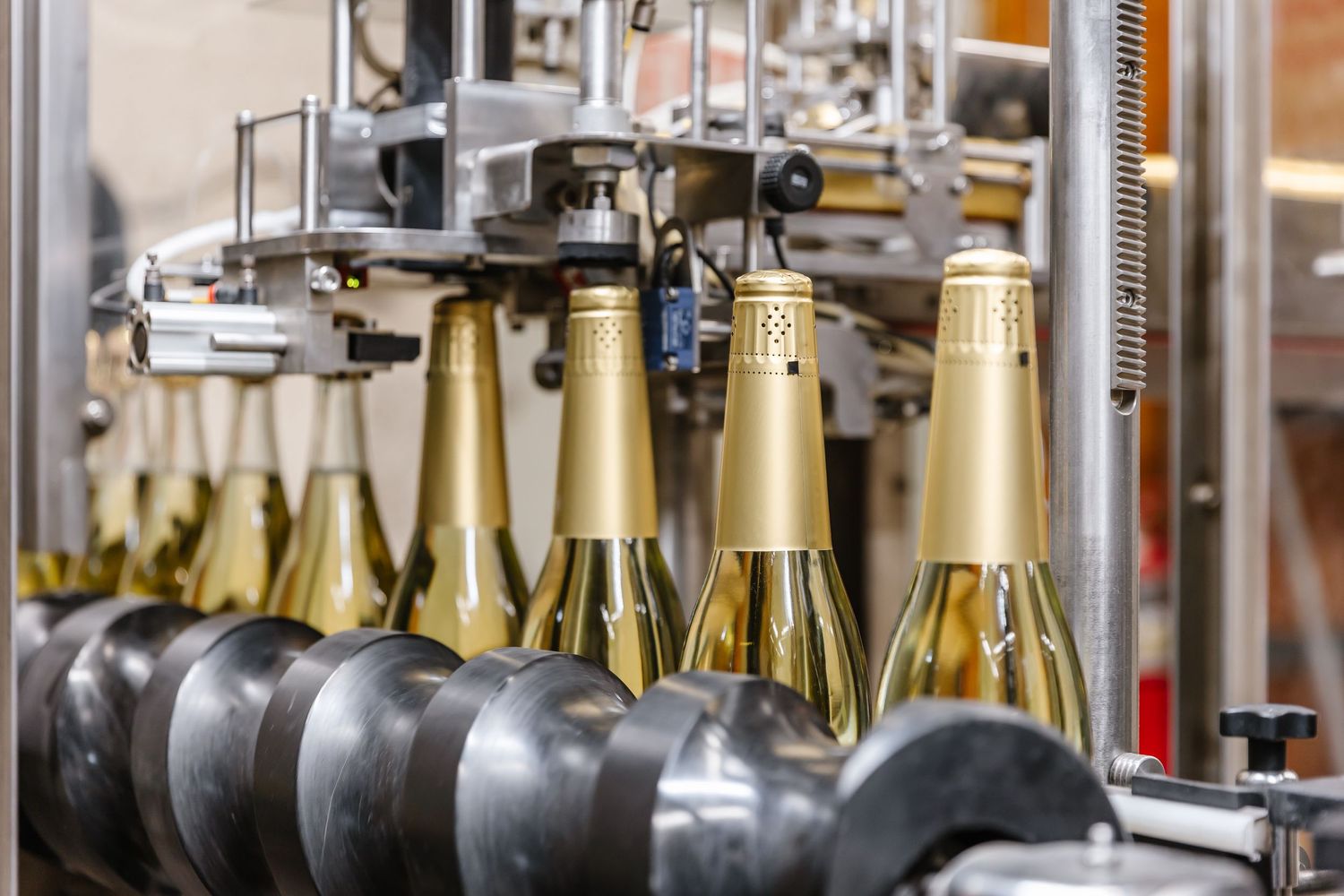 Industrial bottling line with gold champagne bottles moving through automated machinery.