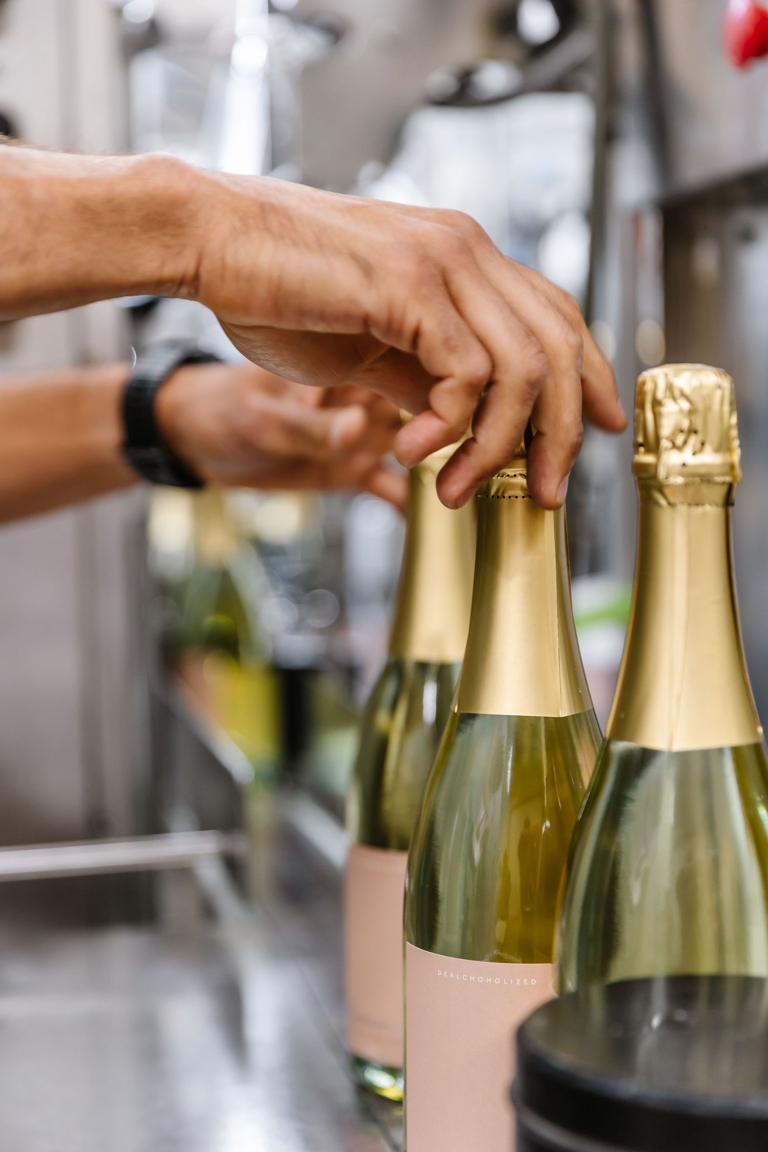 Hands arranging gold champagne bottles in production line.
