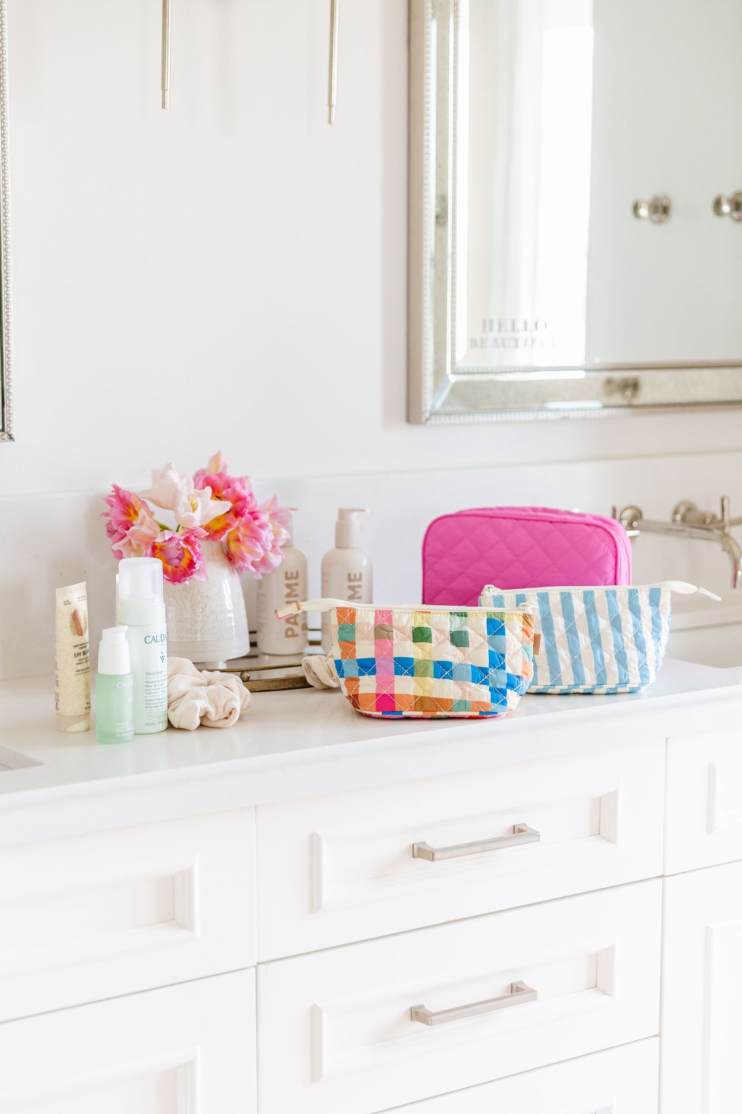 White bathroom vanity counter with pink and blue toiletries scattered across the surface in bright natural light.