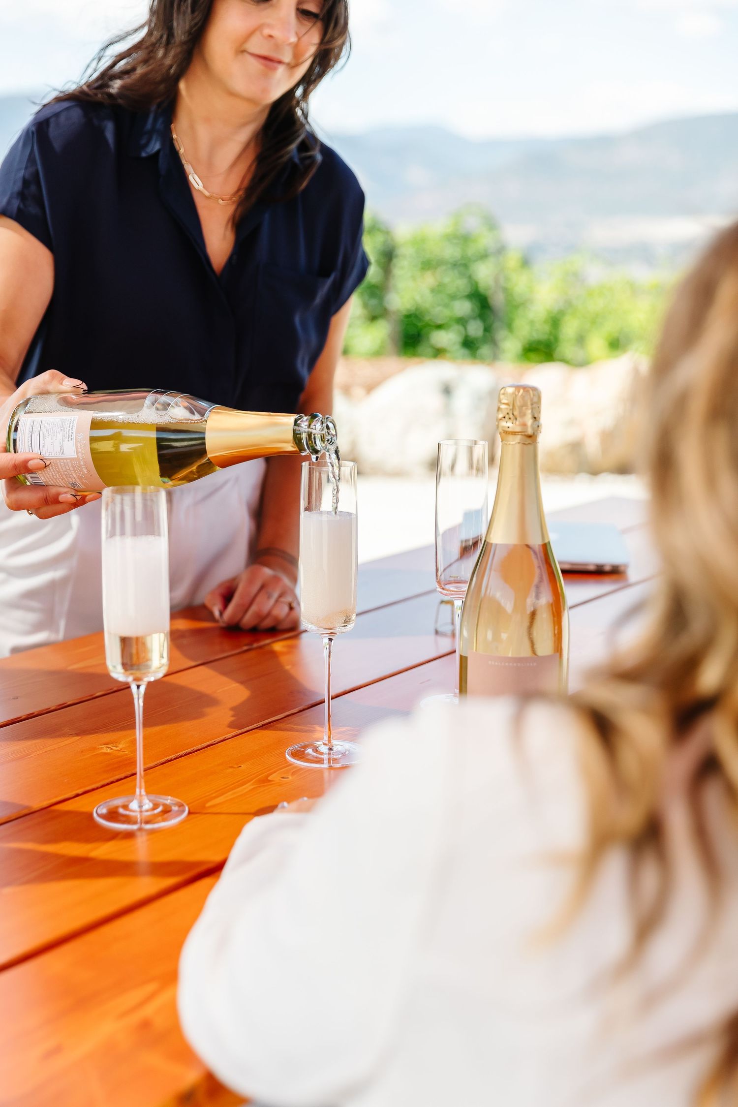 Champagne being poured into flutes at outdoor tasting on wooden table.