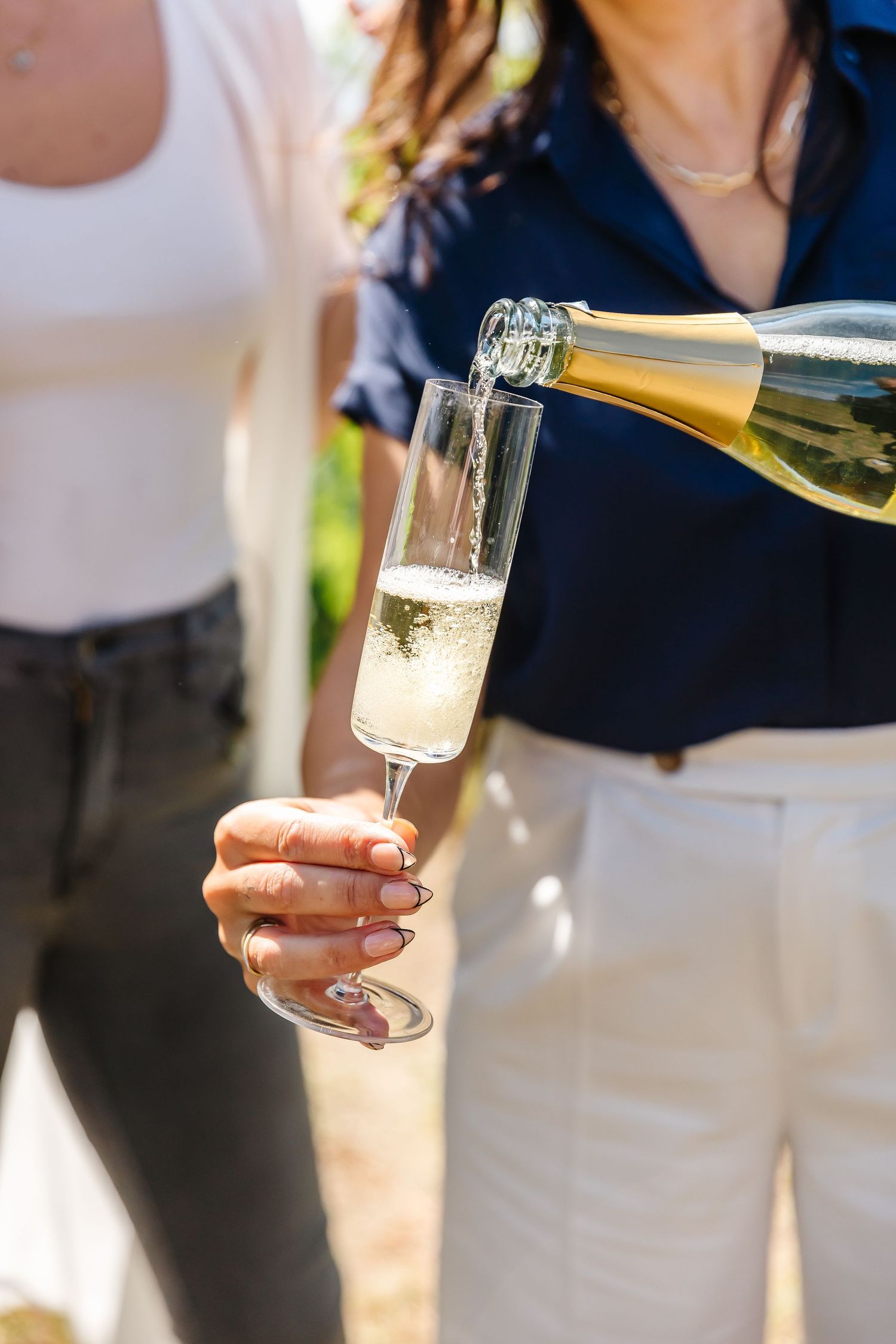 Sparkling wine being poured into champagne flute outdoors in sunlight.