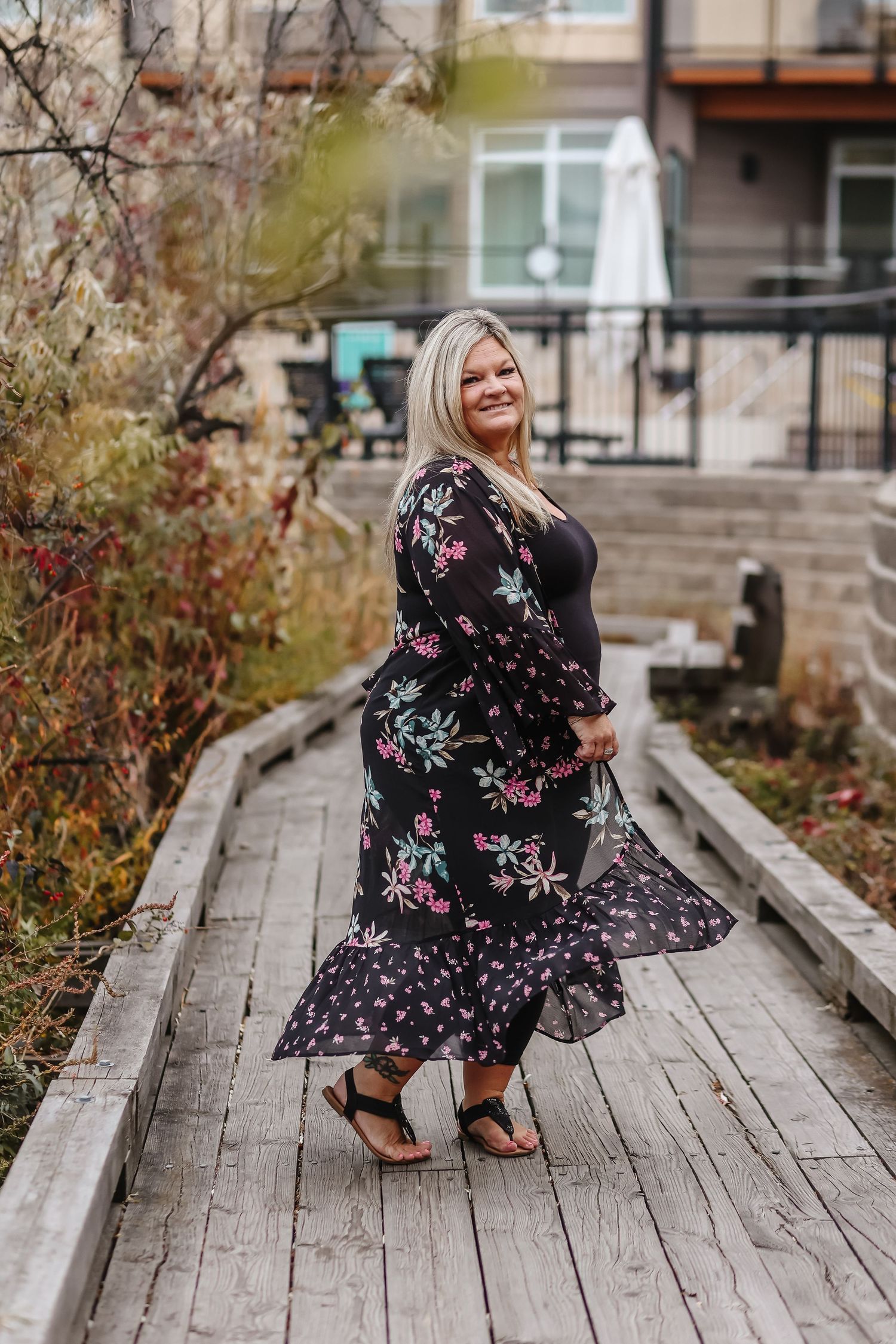 Woman in floral dress posing on wooden boardwalk during autumn.