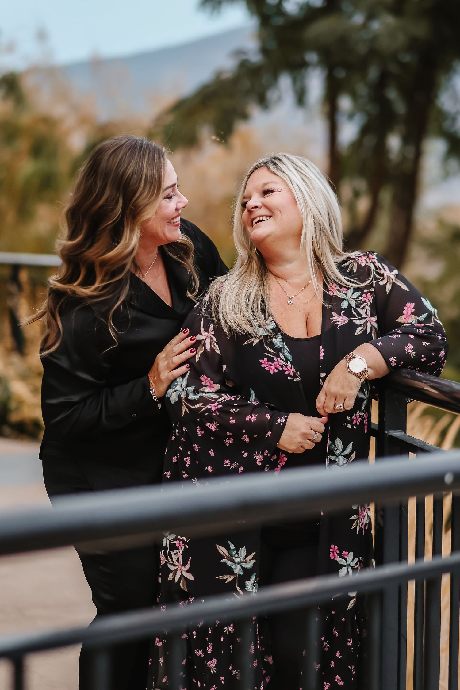 Candid outdoor photos of two friends laughing and embracing in floral outfits.