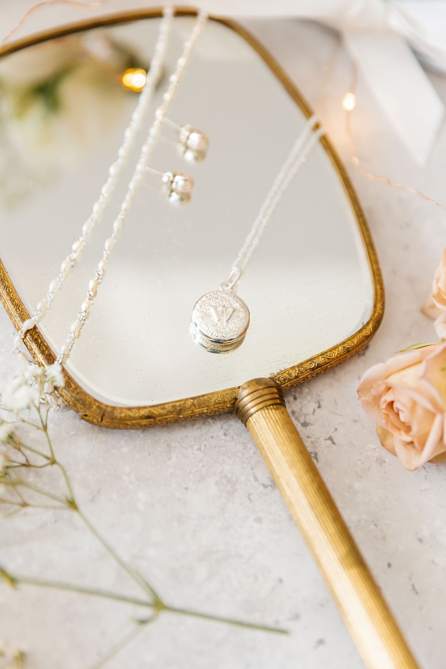 Silver pendant necklace displayed on a vintage gold hand mirror with bokeh lights and pink roses.