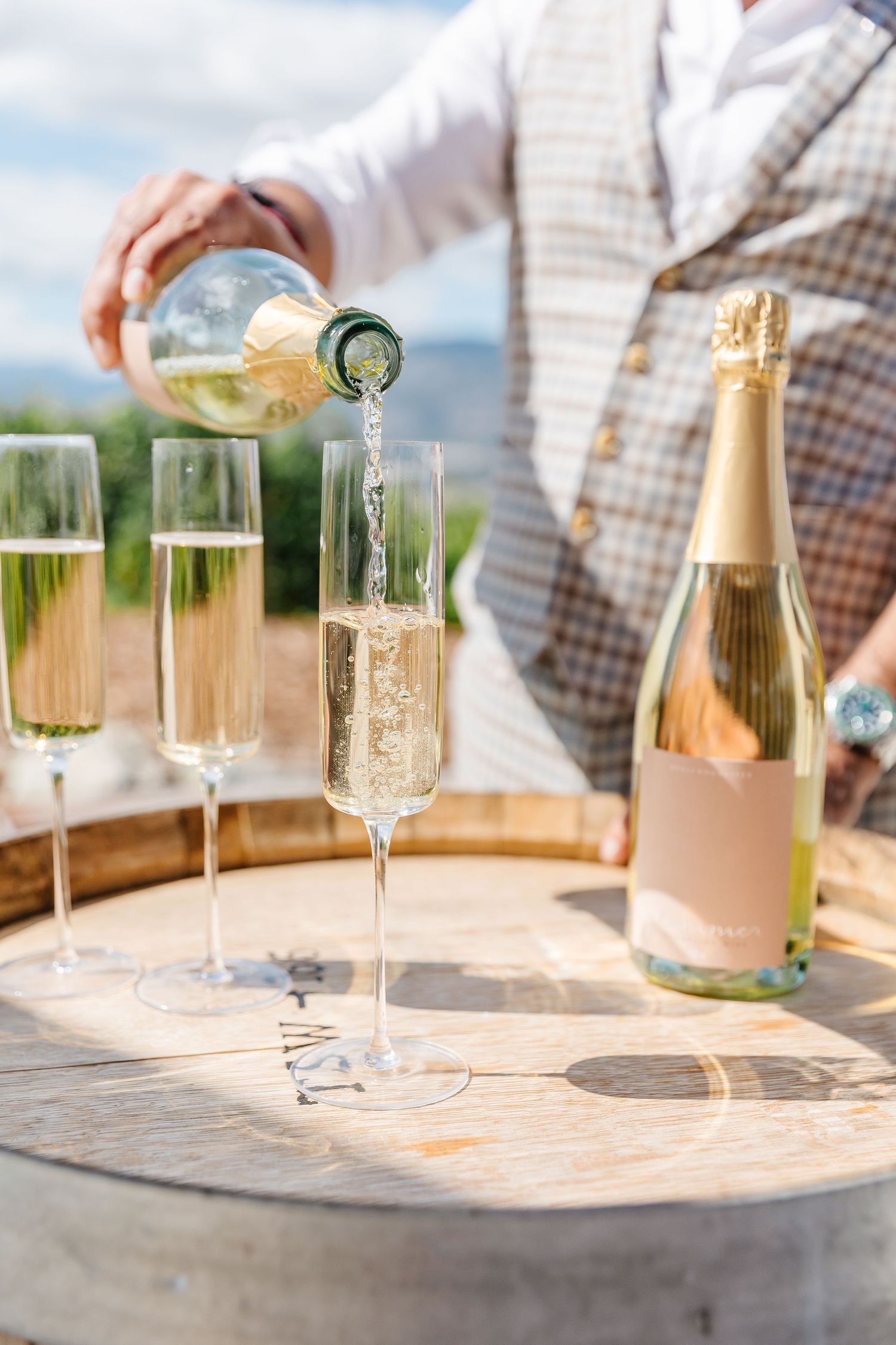 Champagne being poured into elegant flutes on an outdoor table with vineyard views.