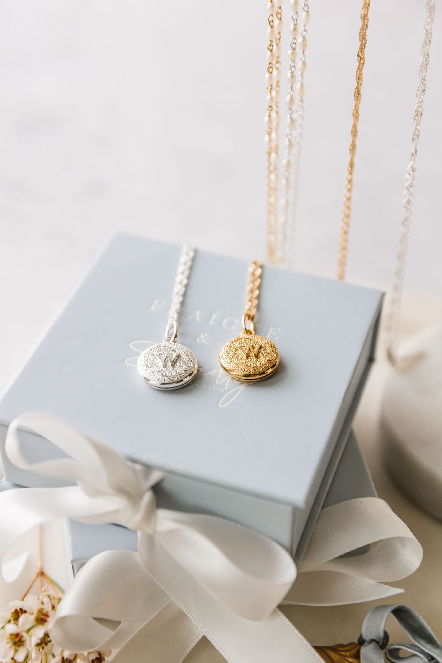 Gold and silver pendant necklaces displayed on gray gift box with white satin ribbon photographed by a West Kelowna photographer