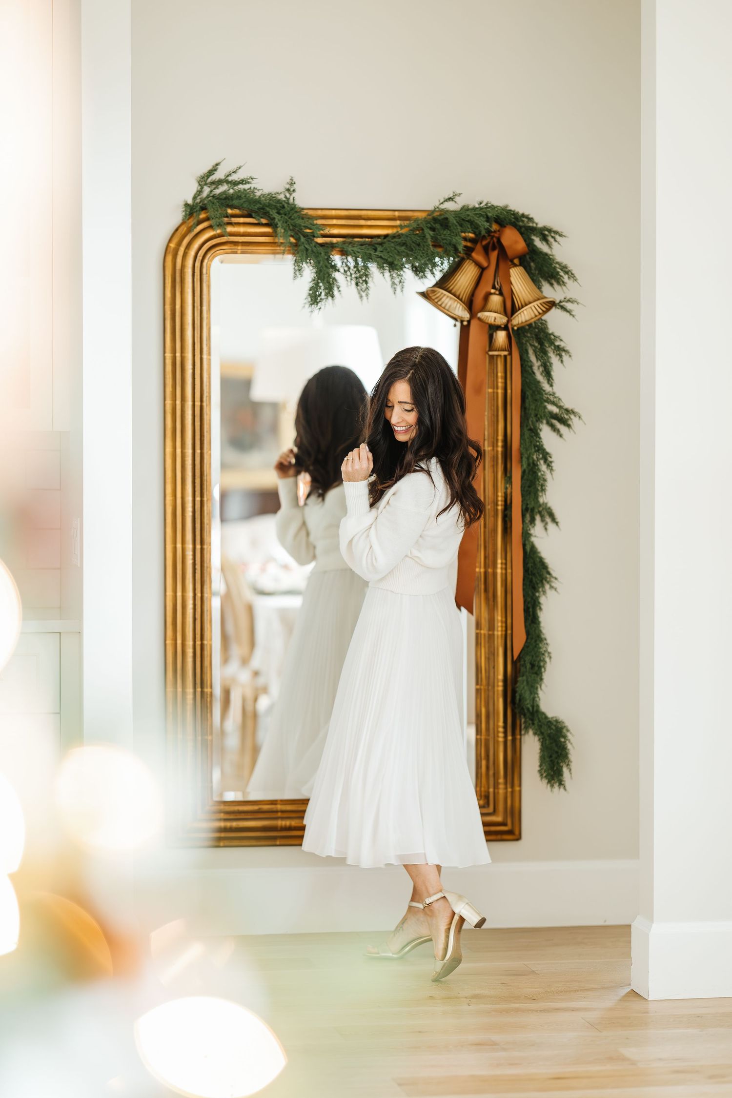 Someone in a white dress dancing and twirling in an elegant room with a gold-framed mirror and holiday garland.