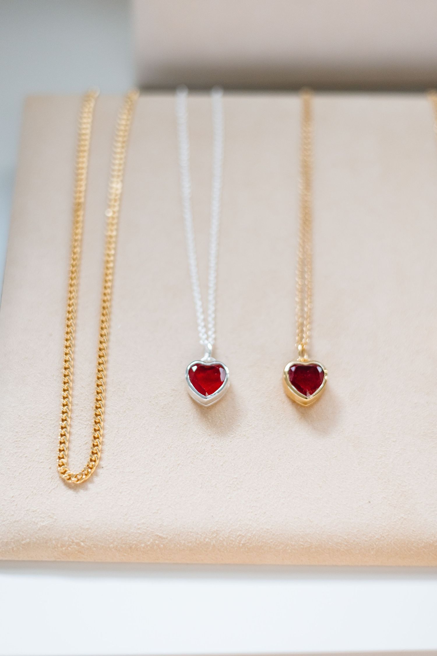 Delicate gold and silver chain necklaces with small heart pendants displayed on a light beige textured surface.
