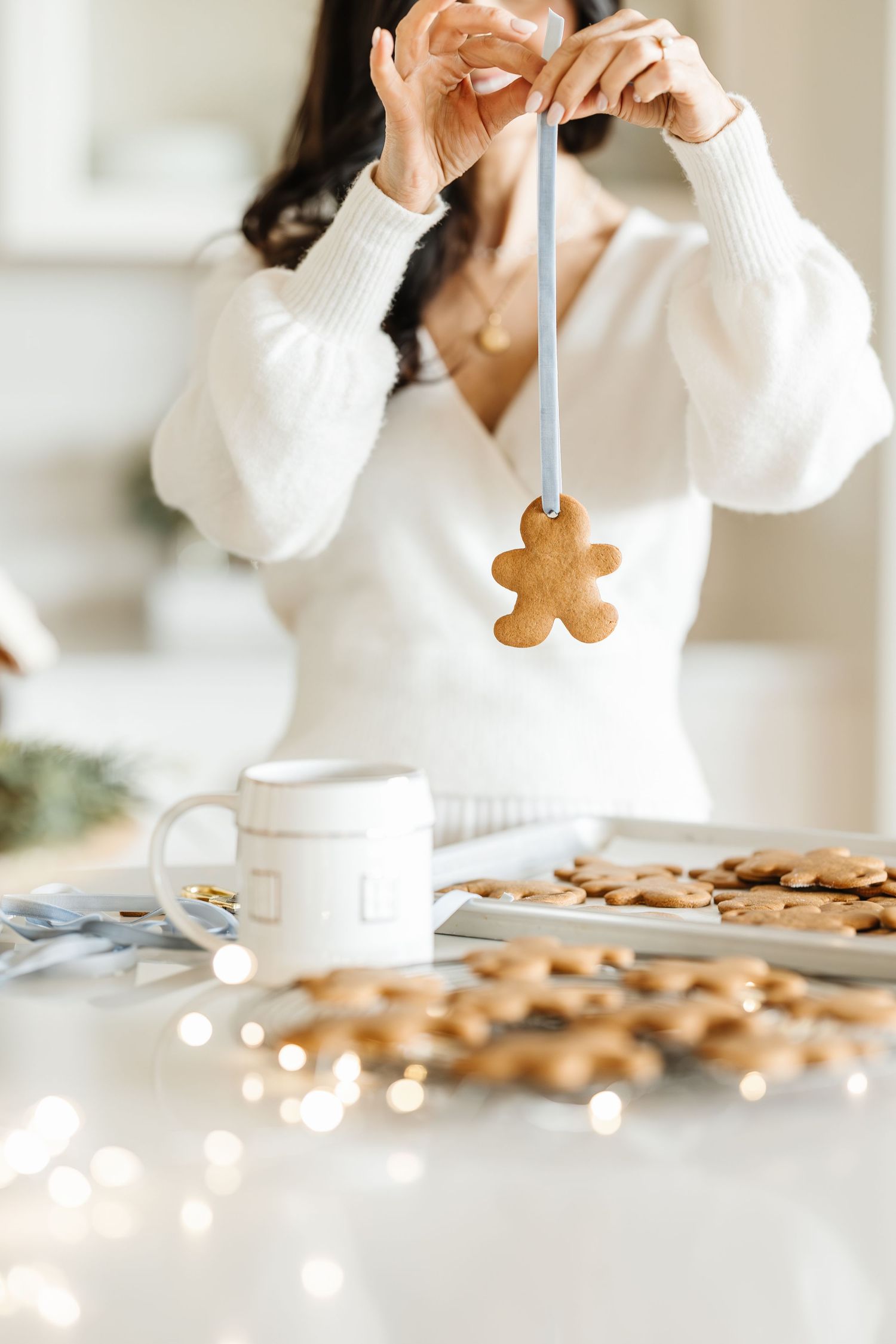 White sweater-clad person holding gingerbread cookie over table with scattered cookies and coffee cup.