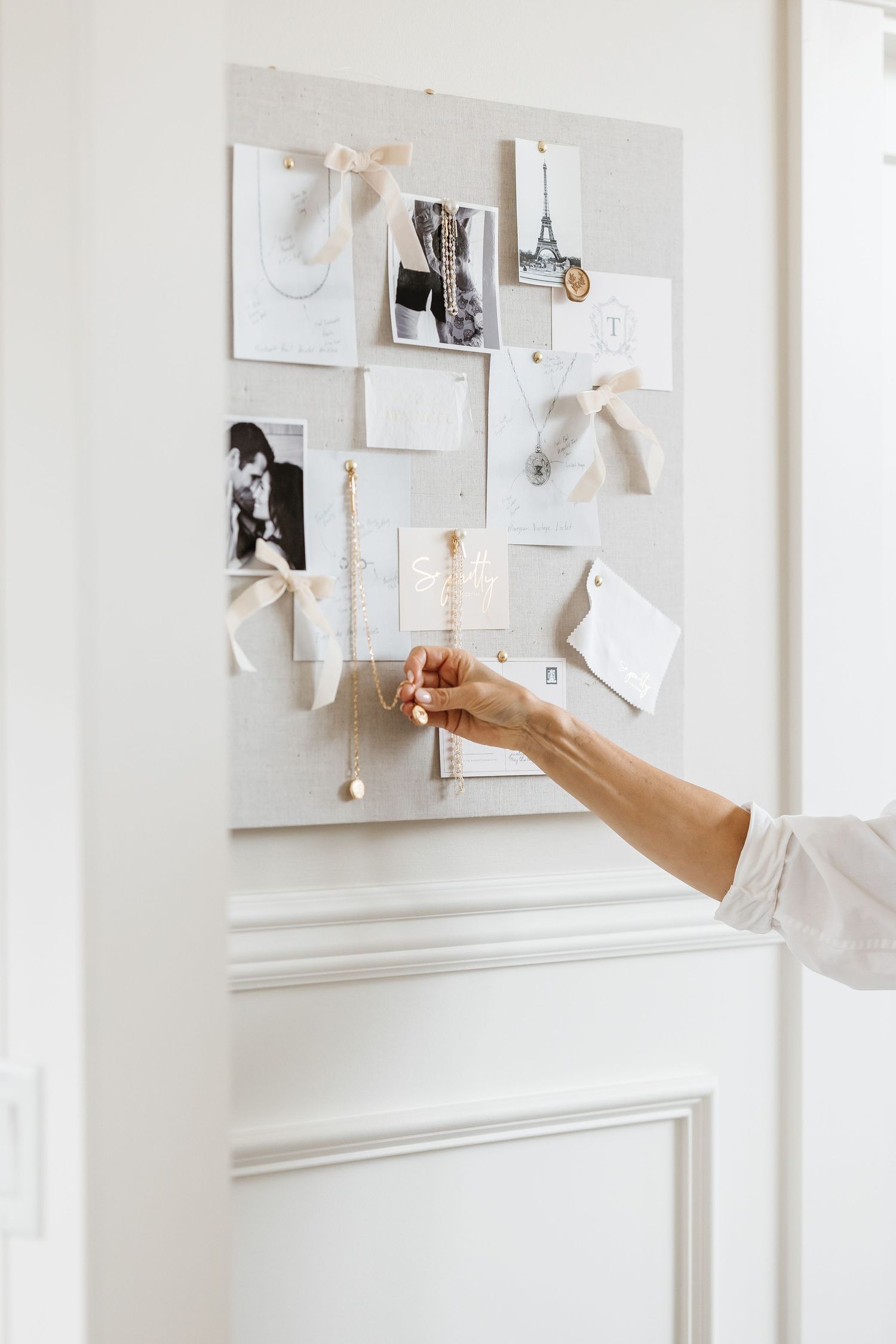 Hand pinning photos and papers to a white vision board wall in natural light for a branding session located in Kelowna, BC