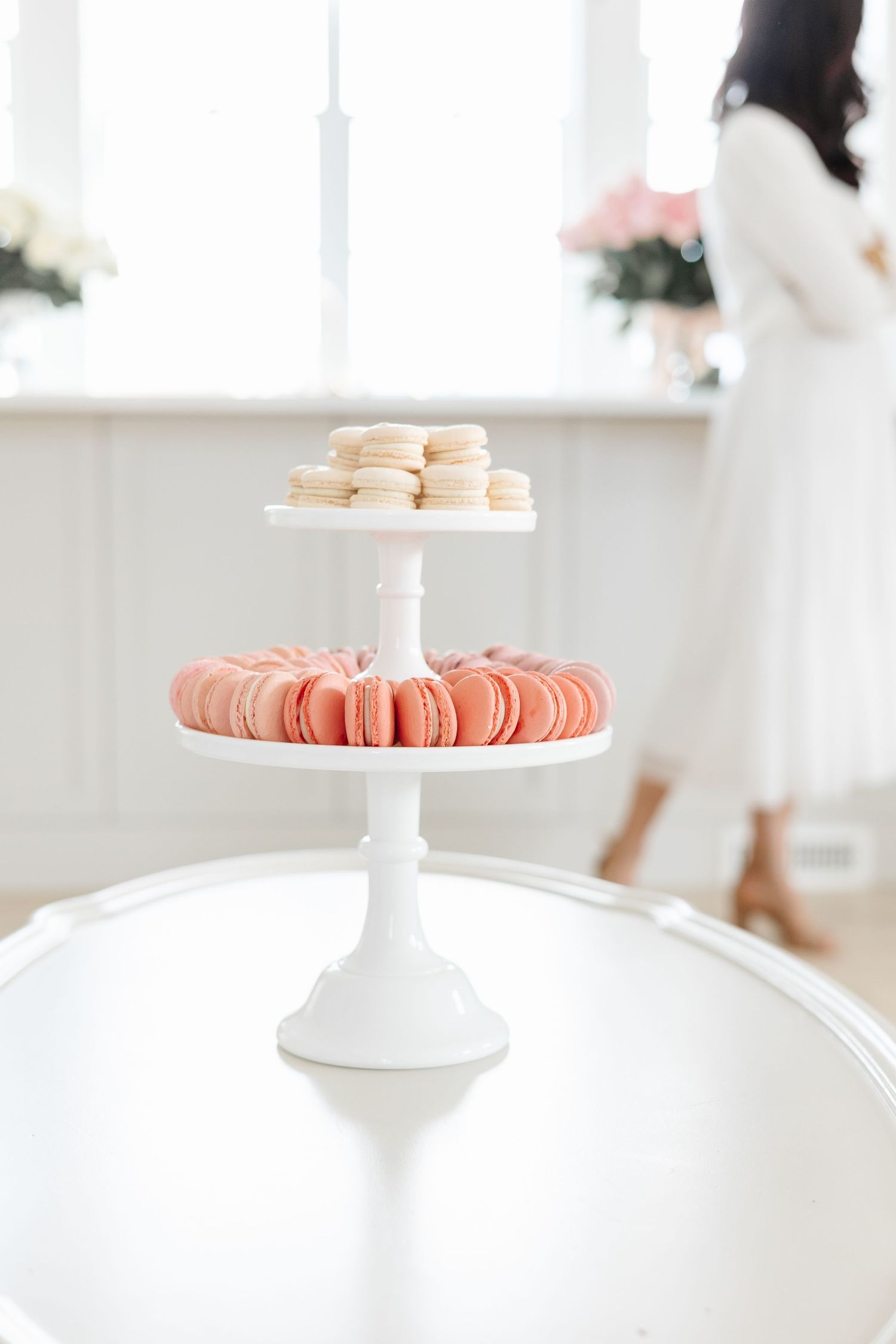 Pink and white macarons are elegantly displayed on white cake stands against a bright white background.