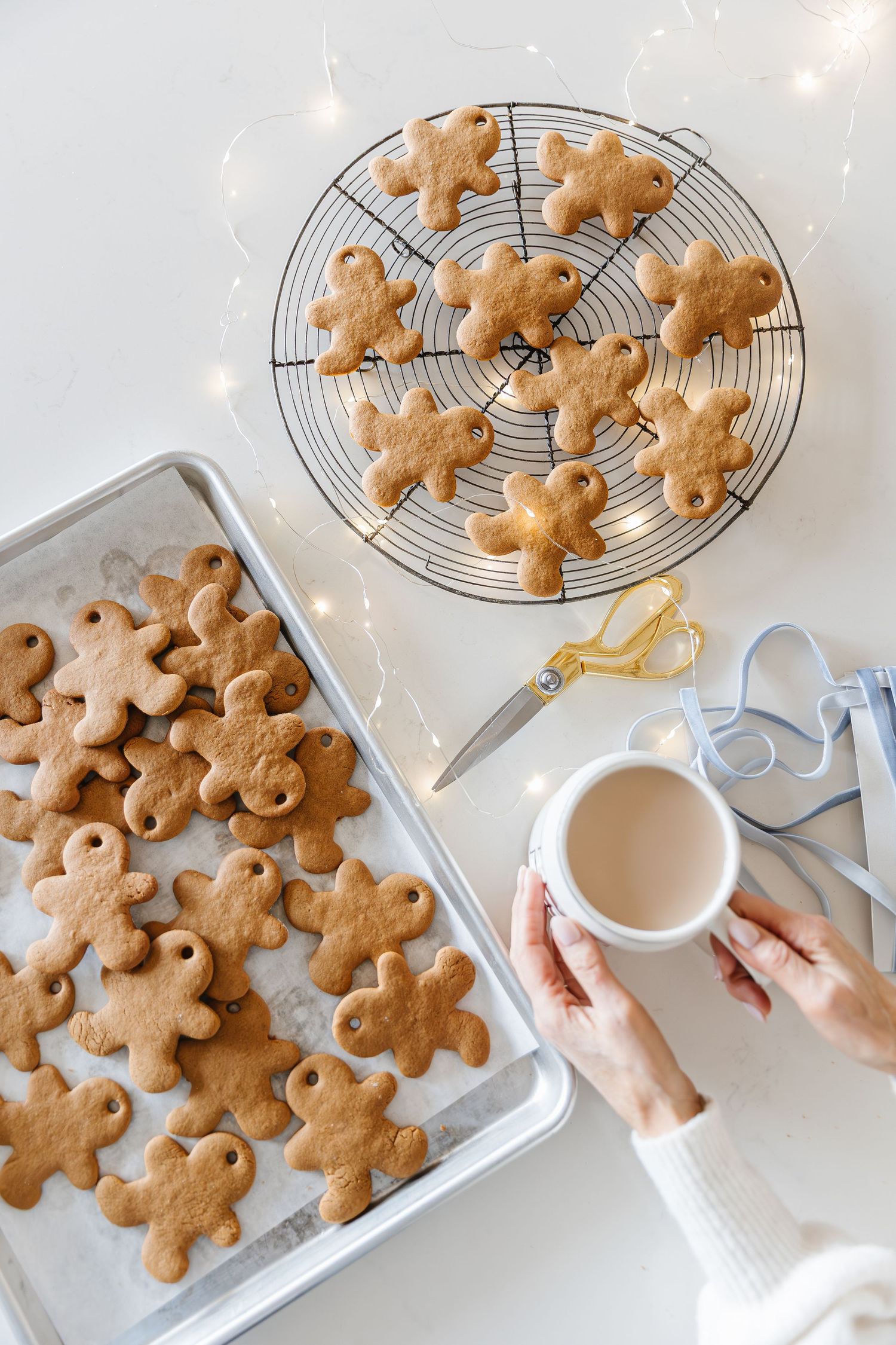 Freshly baked gingerbread cookies cooling on a wire rack with a cup of tea and baking supplies.