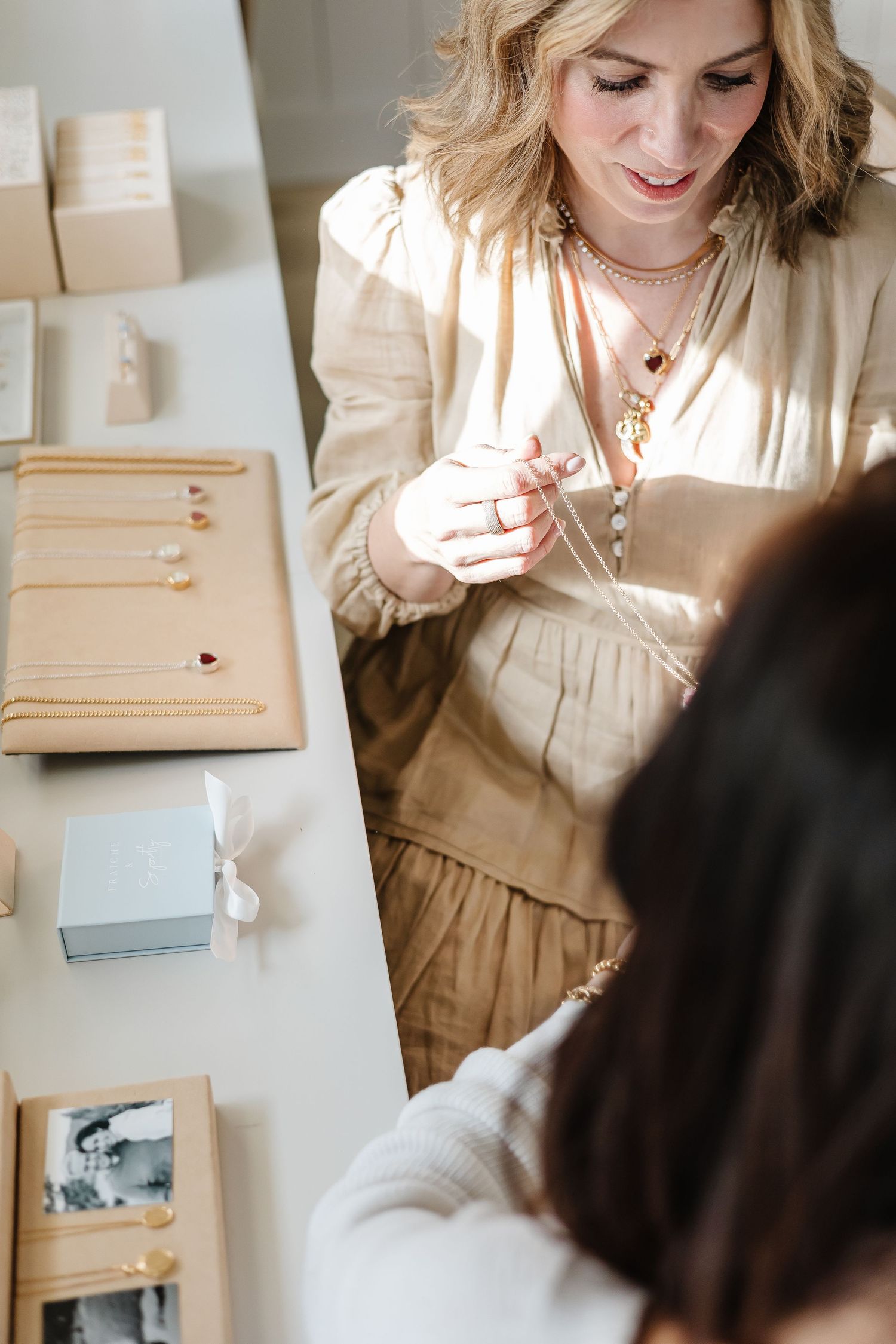 Woman in beige dress preparing gift boxes and packaging materials for a special occasion.