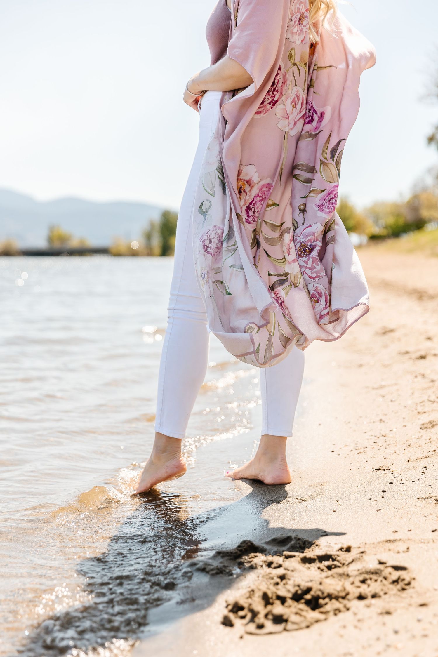 Floral dress and white pants splash in shallow beach water at sunset.