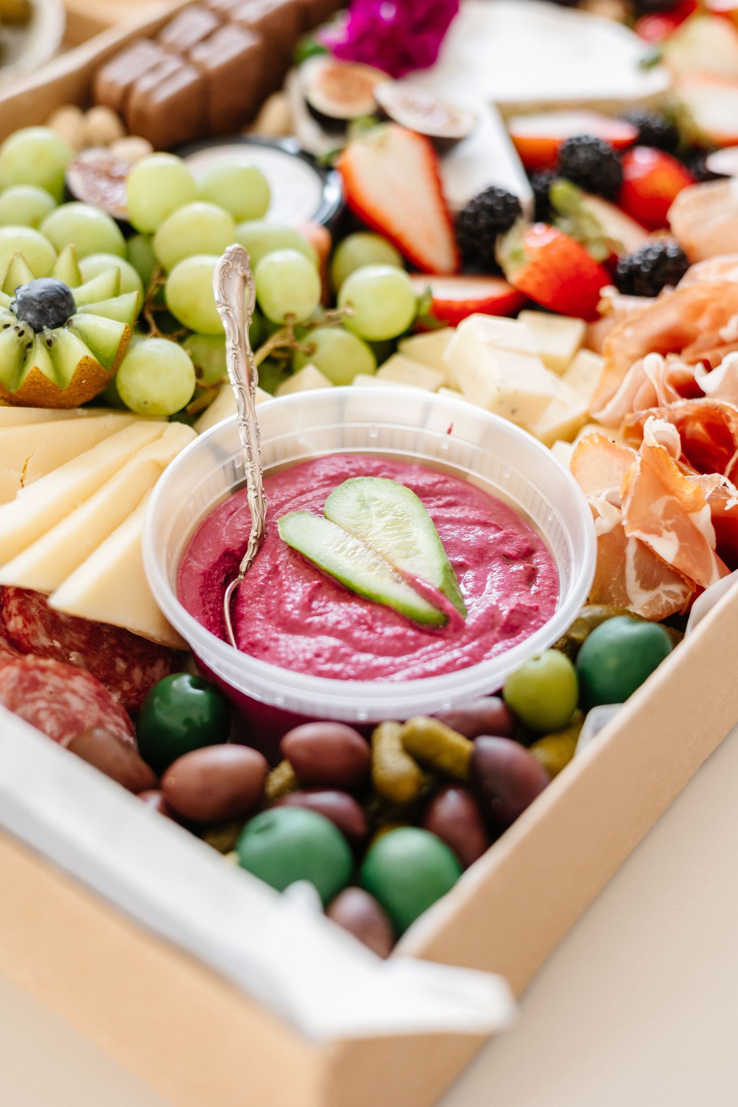 A charcuterie board filled with fresh fruits, meats, cheeses and a vibrant pink dipping sauce.