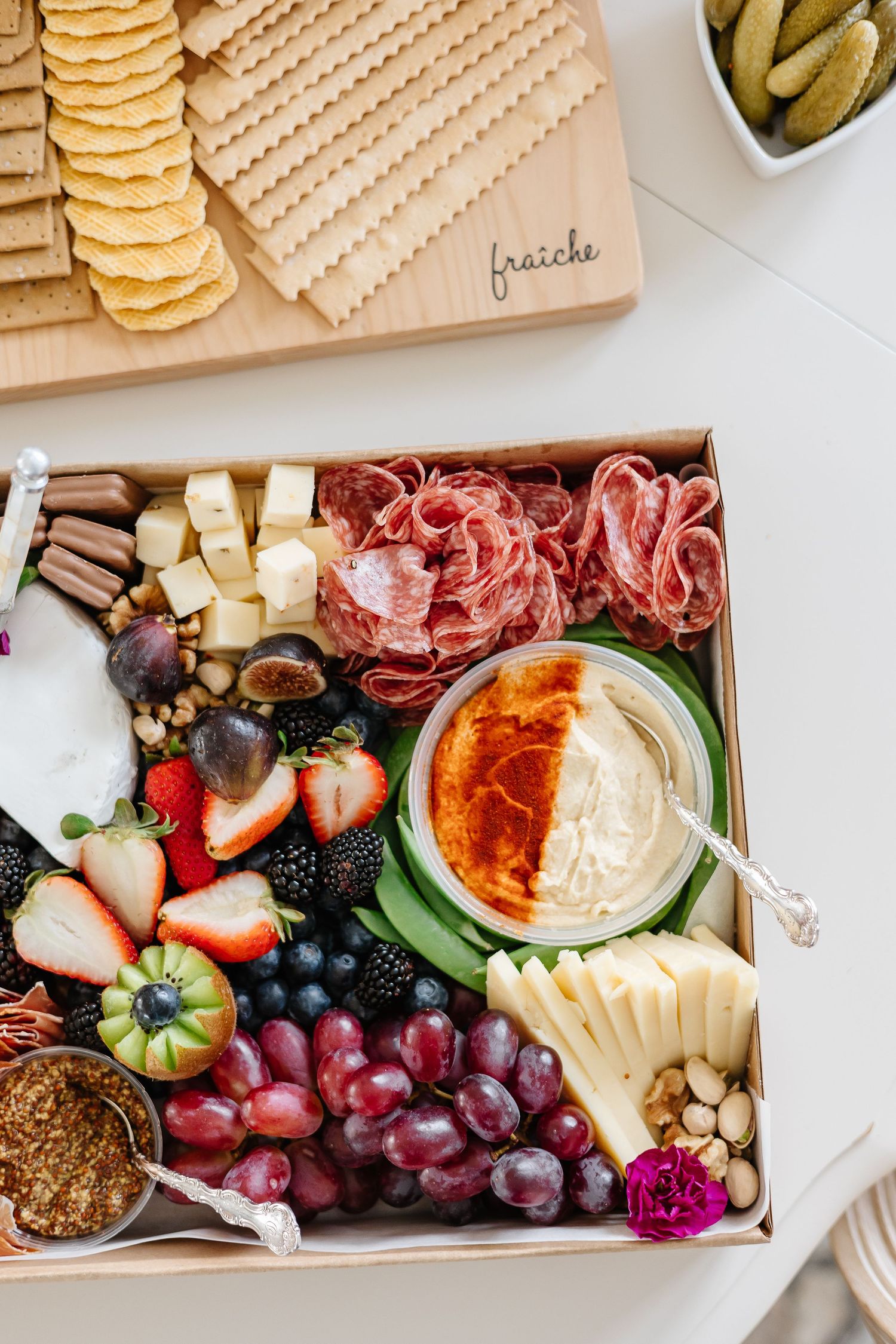 Elegant grazing board with crackers, cured meats, fresh berries, grapes and dipping sauces arranged beautifully.