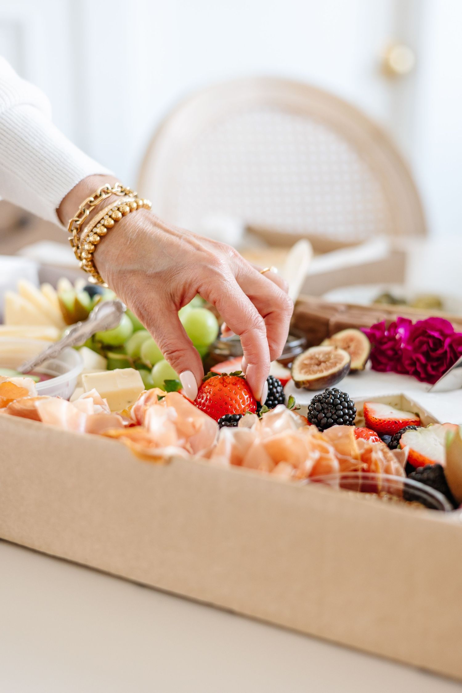 Close-up view of someone arranging food items on a wooden charcuterie board.