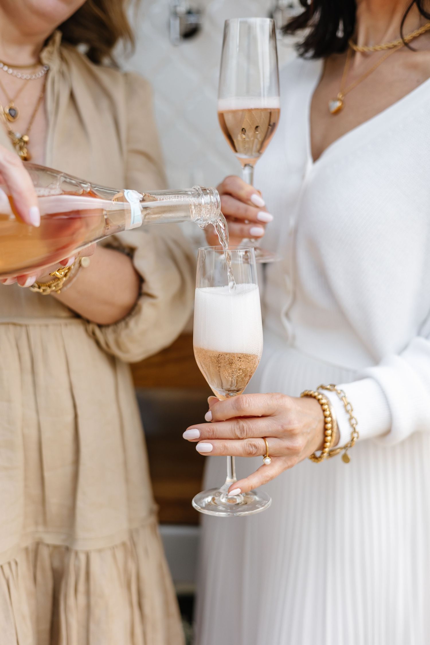 Hands pouring and holding champagne flutes filled with sparkling rosé wine at an elegant celebration.