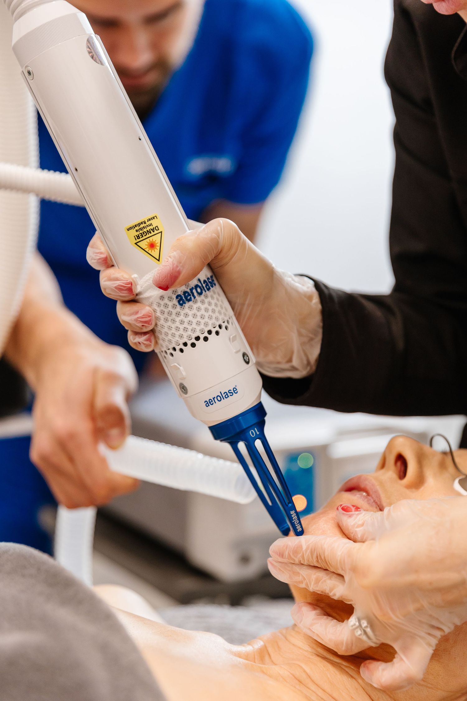 Close-up of hands holding medical device during facial aesthetic procedure on treatment table.