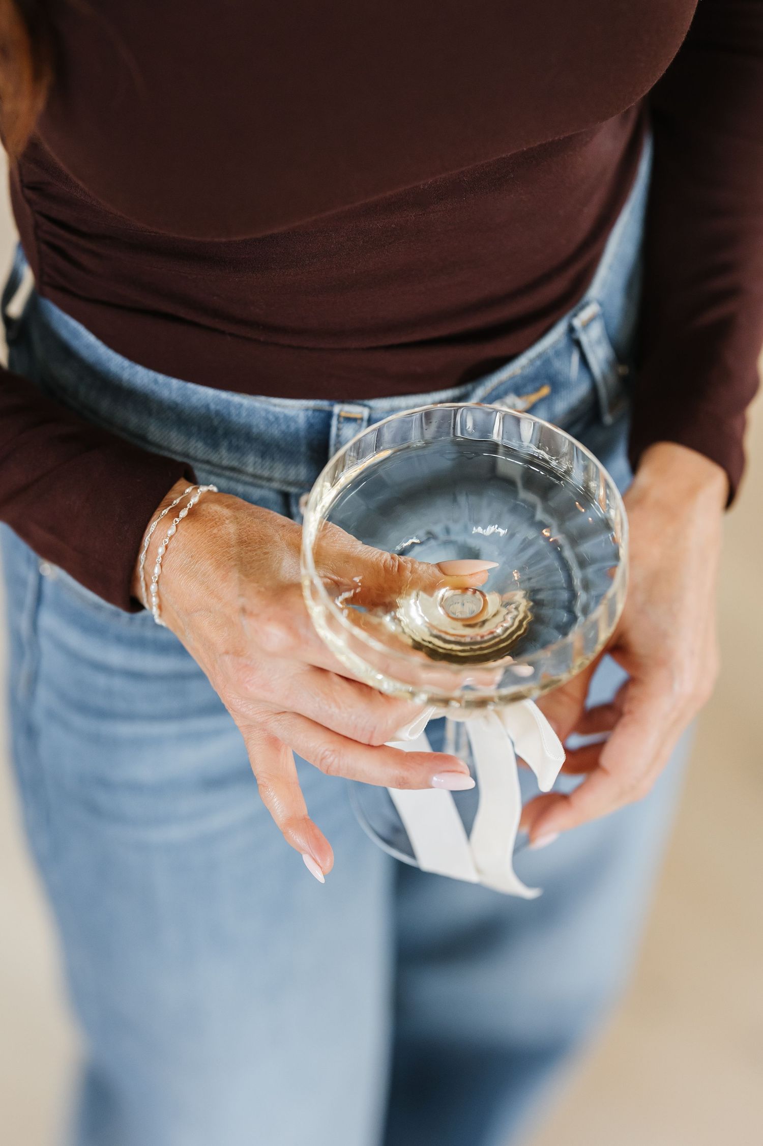 Woman in jeans holding a glass bowl with wedding rings tied with white ribbon at a wedding ceremony.