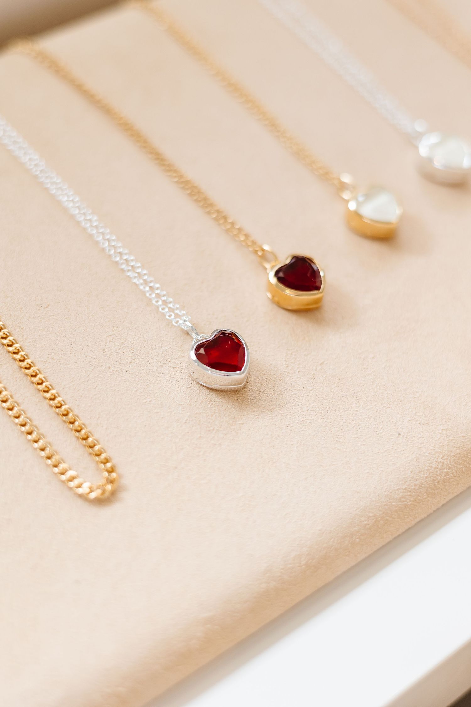 Delicate gold and silver necklaces with heart and pearl pendants displayed on beige fabric.