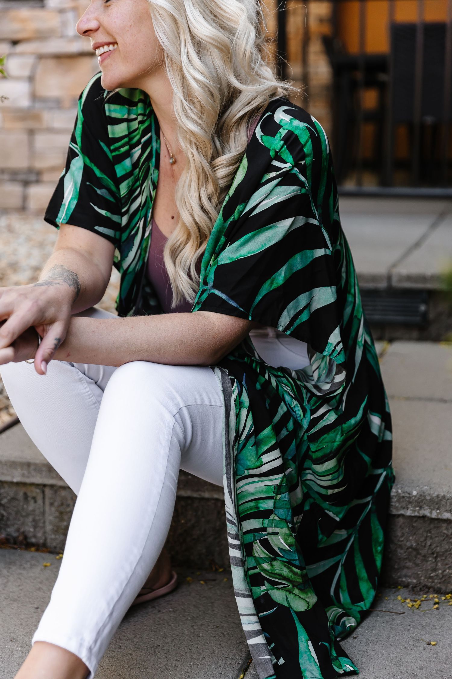 Casual outfit featuring white jeans paired with a tropical print green top in an urban setting.