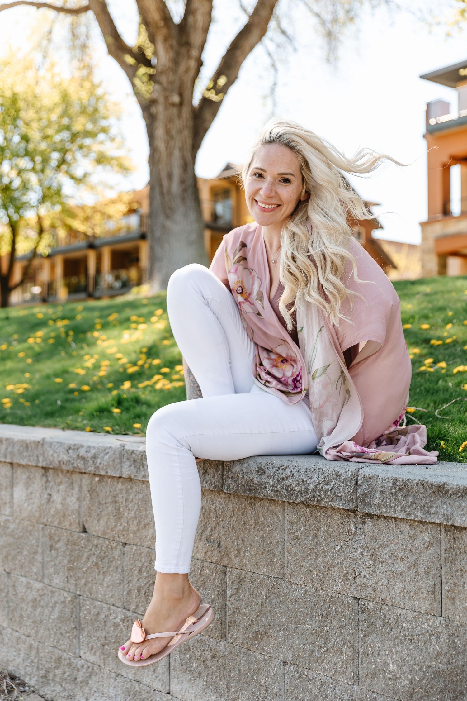 Relaxed outdoor photoshoot with white jeans and pink blouse against autumn trees.
