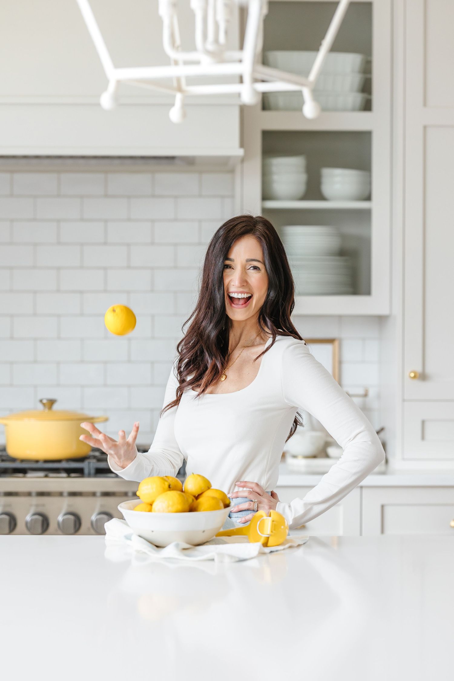 A sequence of four photos showing someone playfully tossing citrus fruit in a bright white modern kitchen.