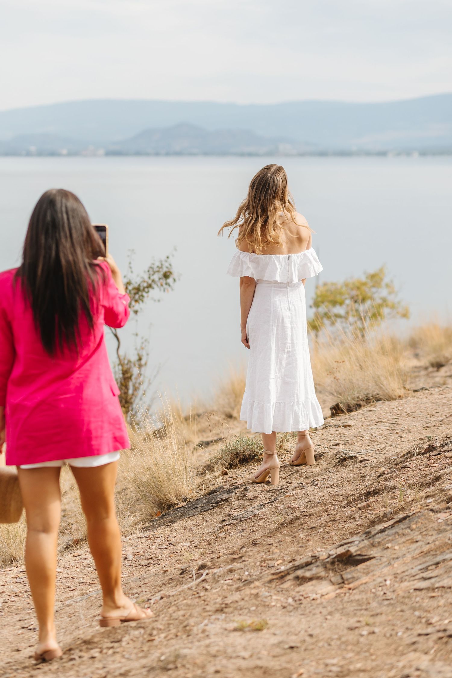 Group walking along hillside trail overlooking serene lake and mountain views.