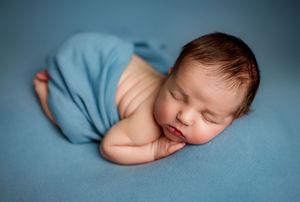 Newborn baby sleeping peacefully wrapped in a soft blue blanket on a blue background.
