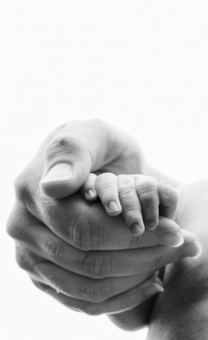 Black and white photo of a newborn baby's tiny hand gently held within large adult hands.