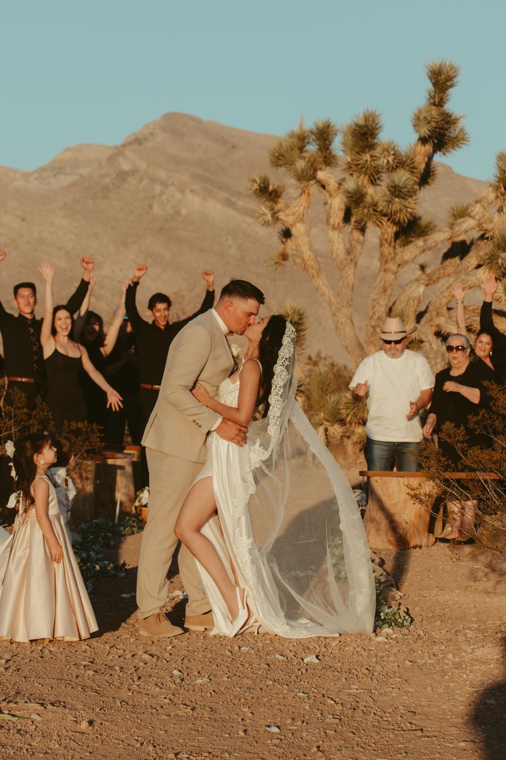 A desert wedding celebration with couples dancing and embracing among Joshua trees at sunset.