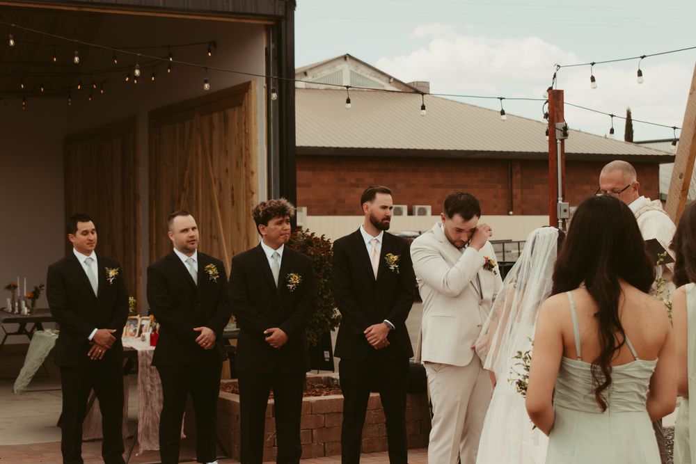 A wedding party stands in a line at an outdoor venue with string lights overhead and warm vintage tones.