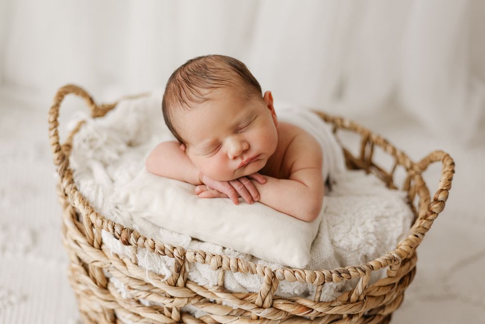 Baby boy with his head resting on his hands in a basket