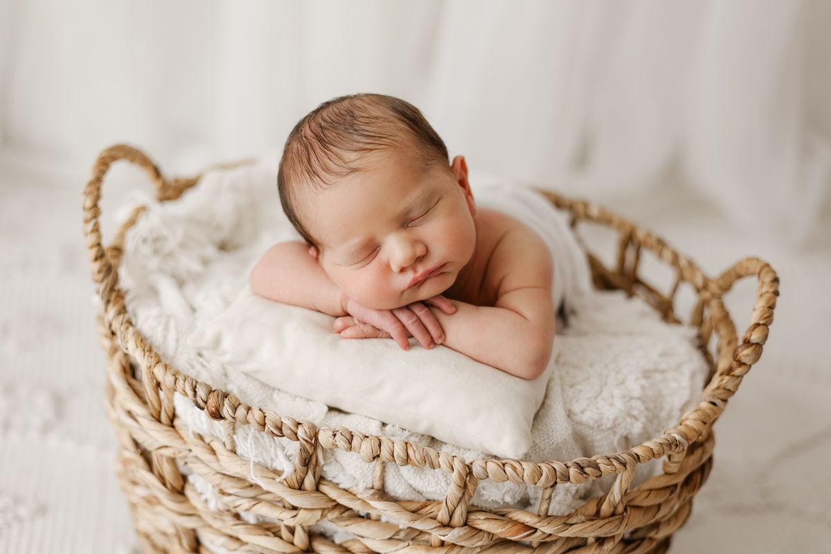 Baby boy with his head resting on his hands in a basket