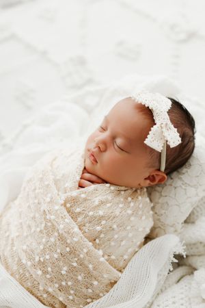 newborn baby wrapped in white basket with white bow