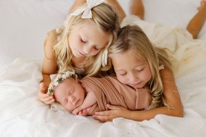 sisters snuggling newborn baby girl