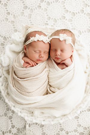 newborn twin girls wrapped up in a white basket