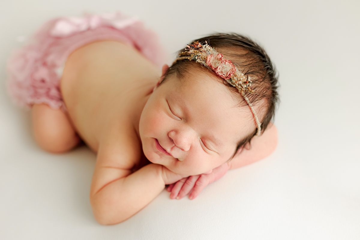 Baby girl laying her head on her hands on a white blanket