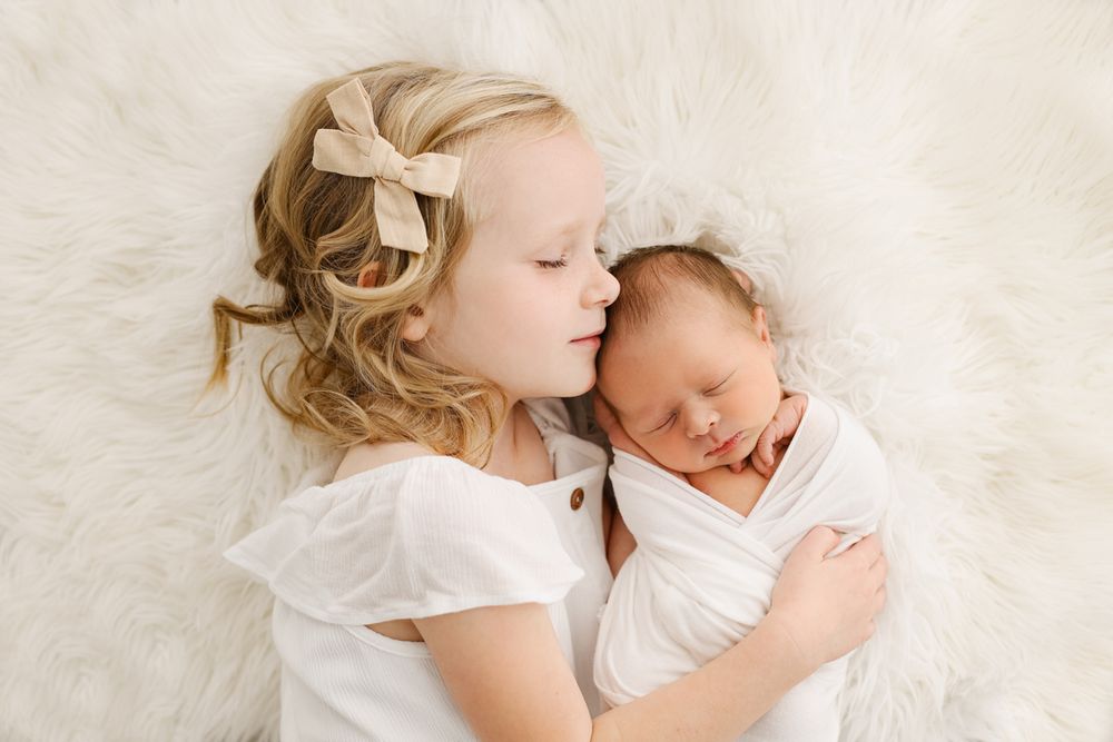 Little girl snuggling her baby brother on a white fur blanket
