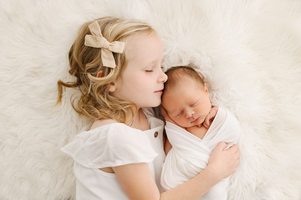 Little girl snuggling her baby brother on a white fur blanket