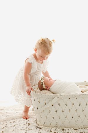 toddler looking at baby in white basket
