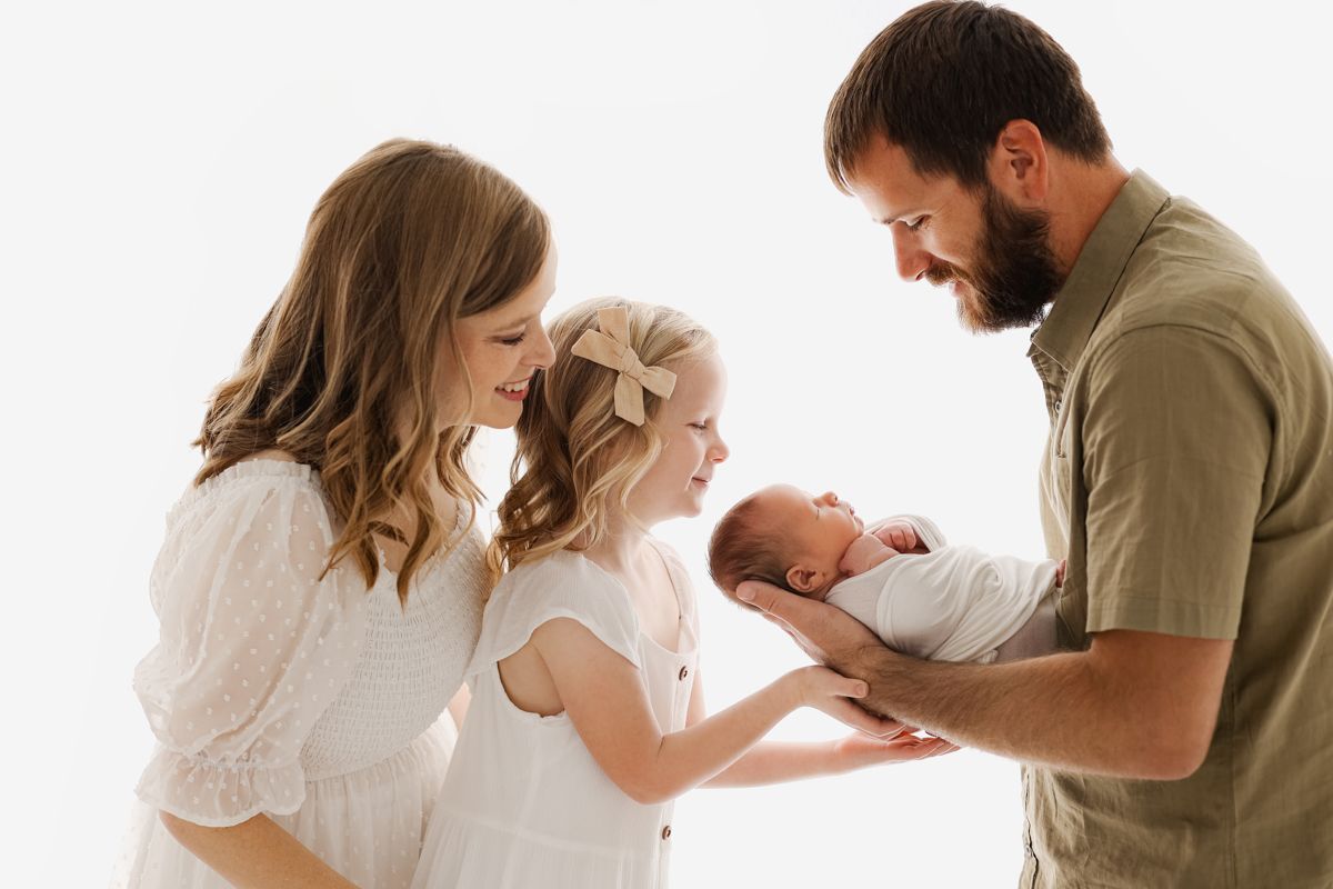 Mom and dad backlit in a white studio smiling at daughter and baby boy