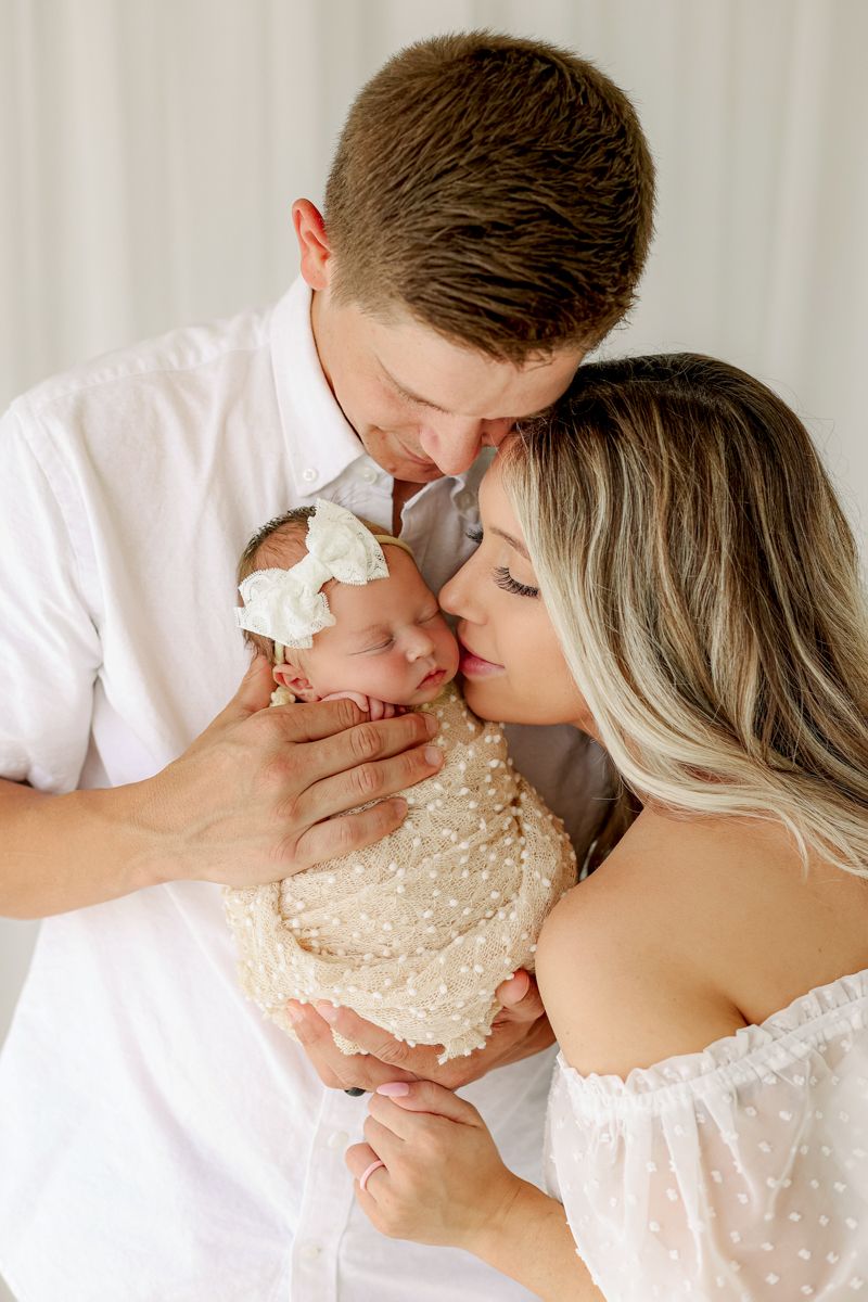 Mom and dad holding a baby, mom kissing her cheek