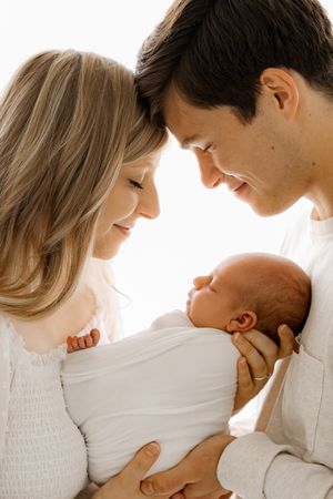 mom and dad backlit in a white studio holding on to a baby boy