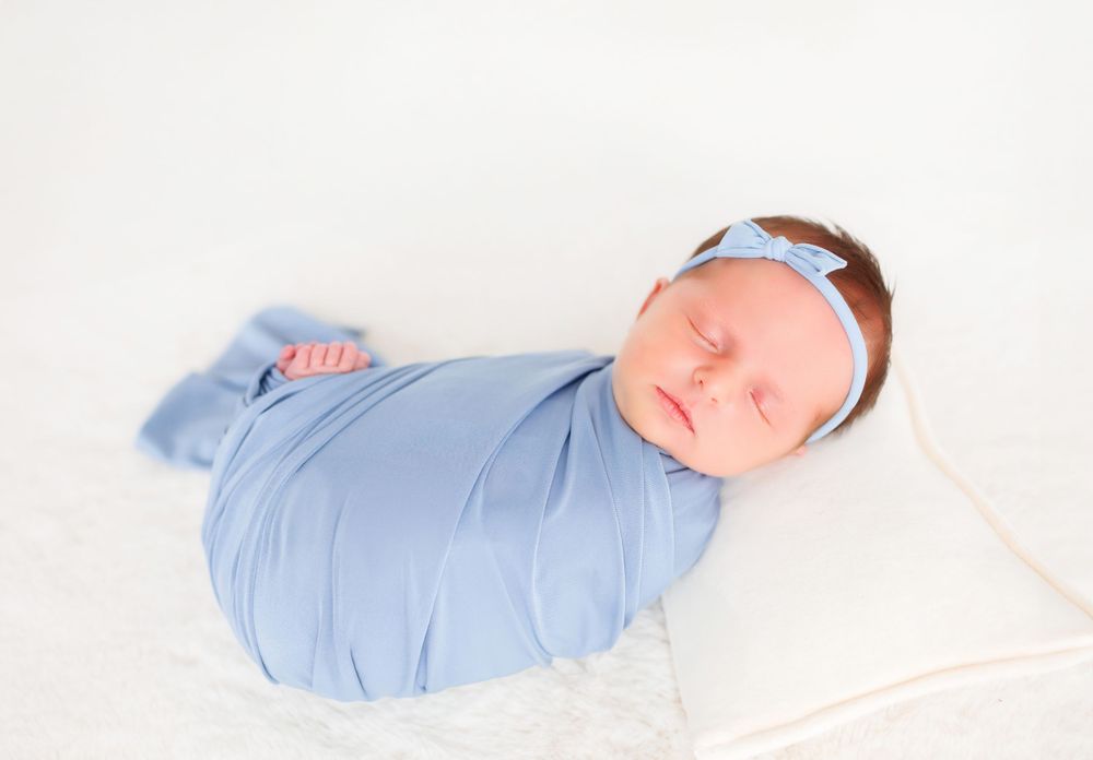 Sleeping newborn wrapped in soft blue swaddle with delicate headband.