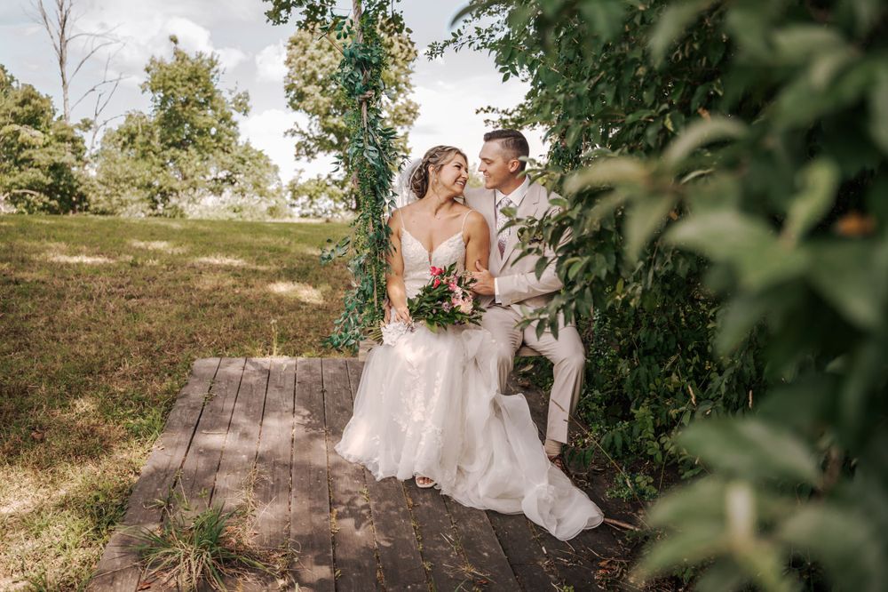 Outdoor wedding portrait of couple on wooden platform with greenery arch.